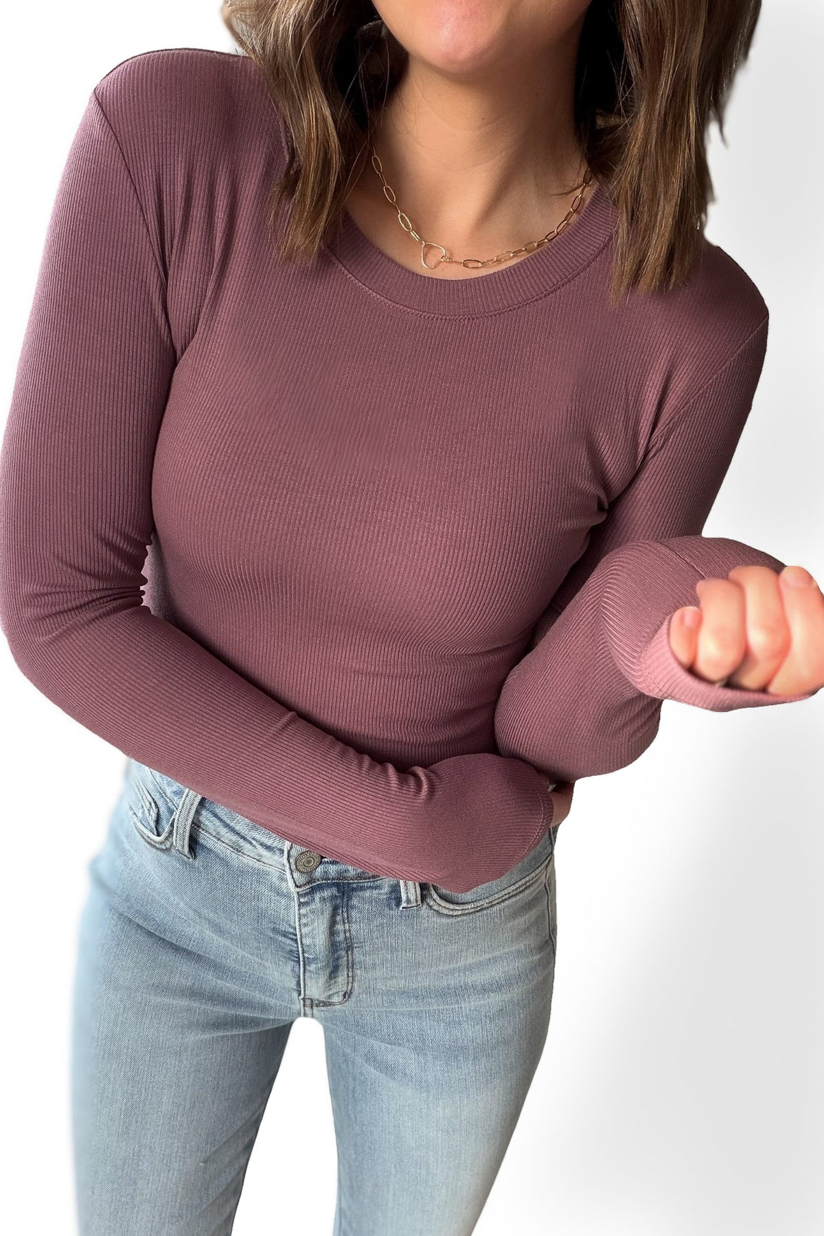 Person wearing a mauve long-sleeve top and light blue jeans on a white background