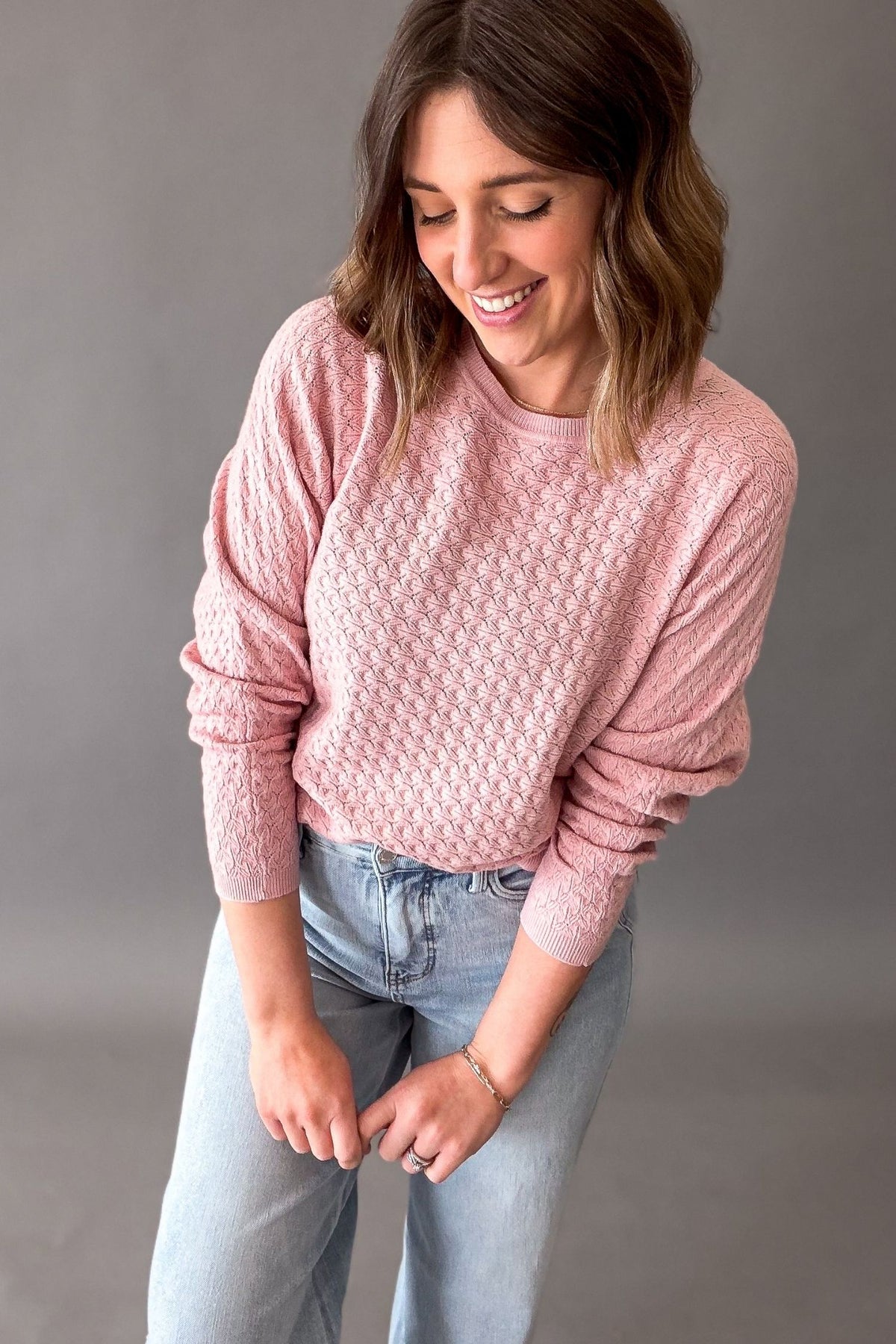 Woman wearing a rose pink pointelle knit sweater with lightweight soft fabric and stretch, casual everyday sweater for women