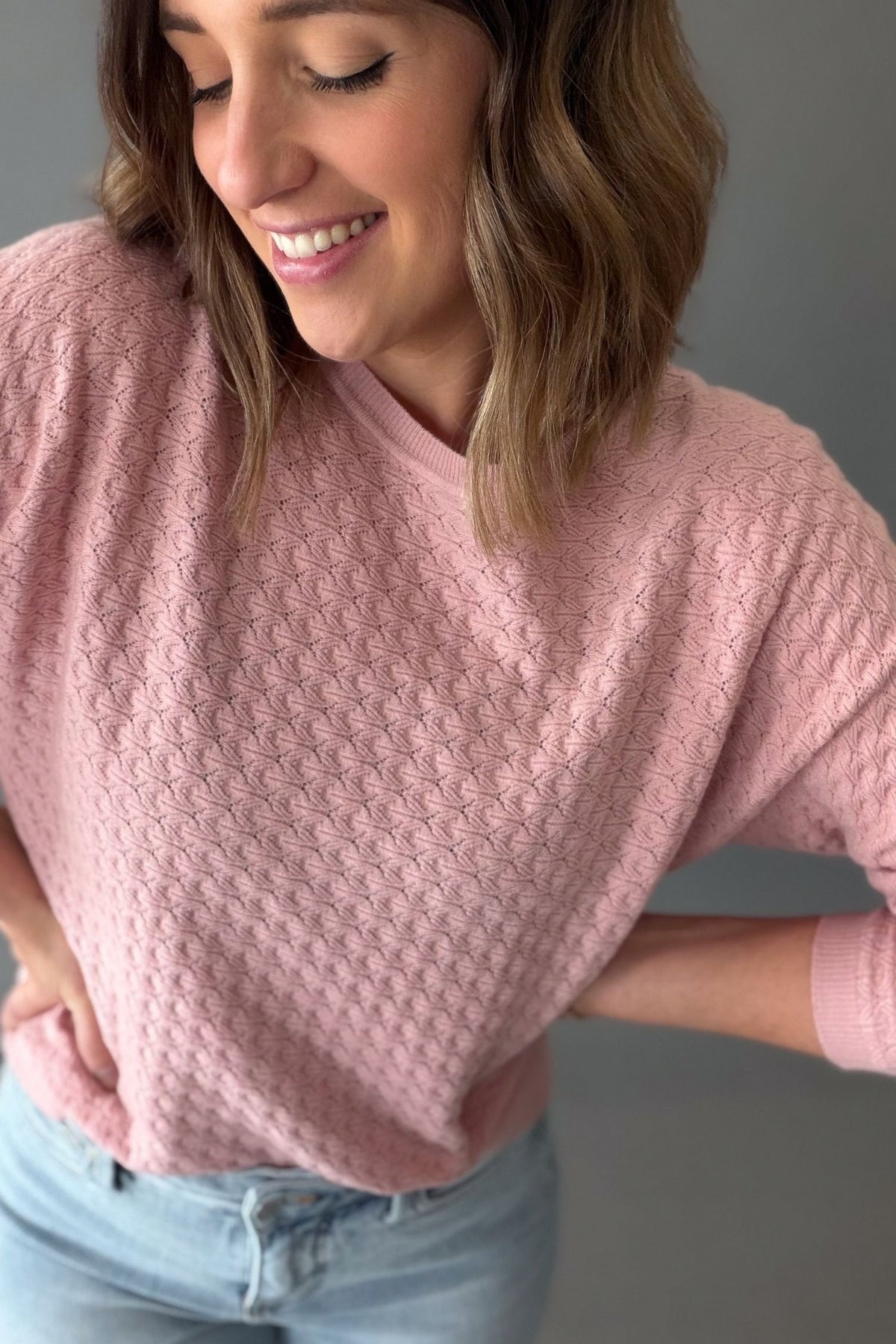 Woman wearing a rose pink pointelle knit sweater showing the soft texture