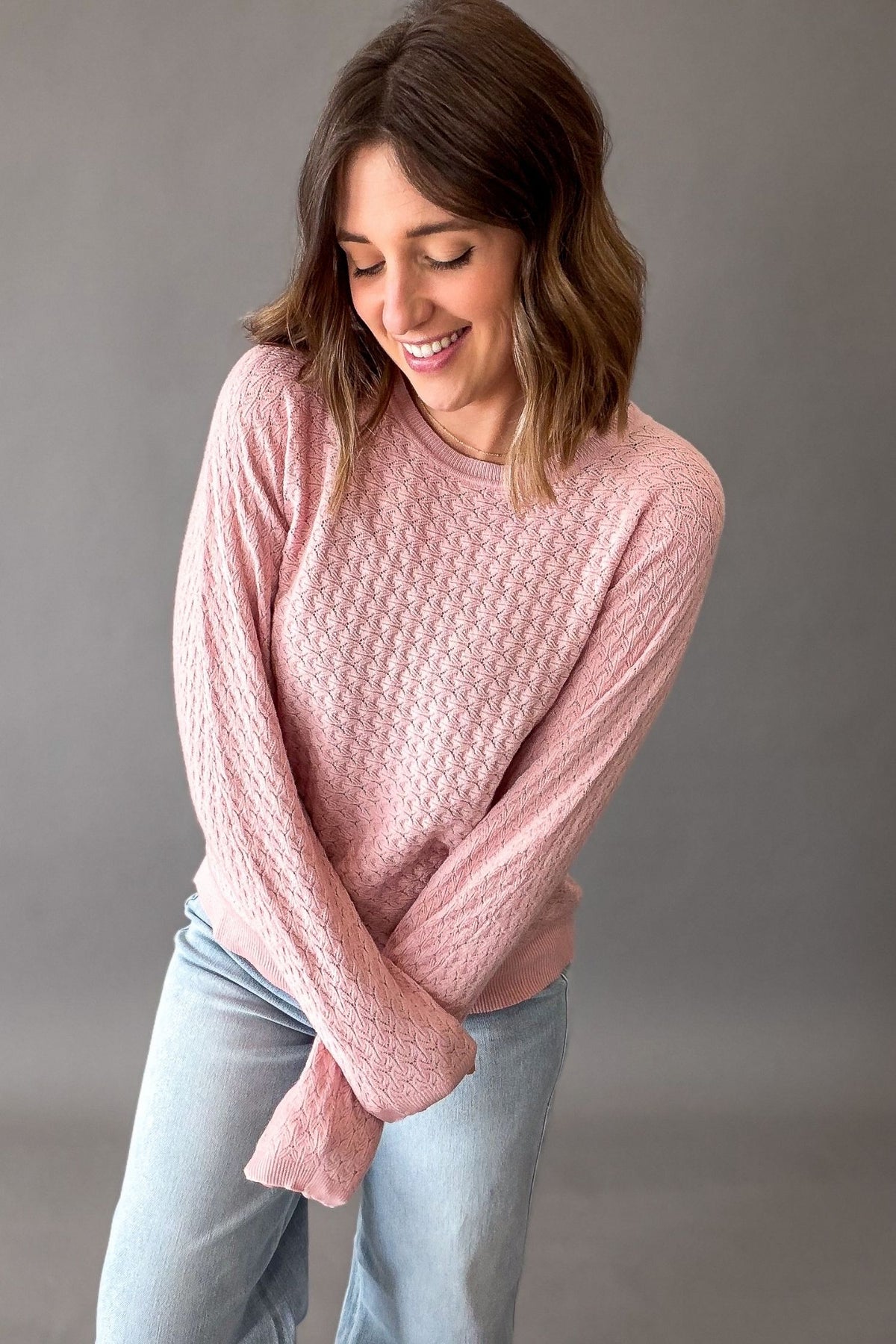 Woman wearing a rose pink pointelle knit sweater showing the long sleeve length