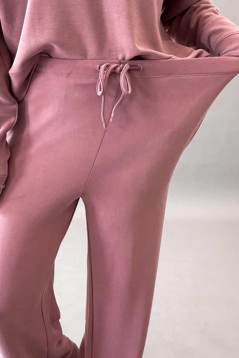 woman wearing a rose pant and sweatshirt set showing the stretch in the waistband.