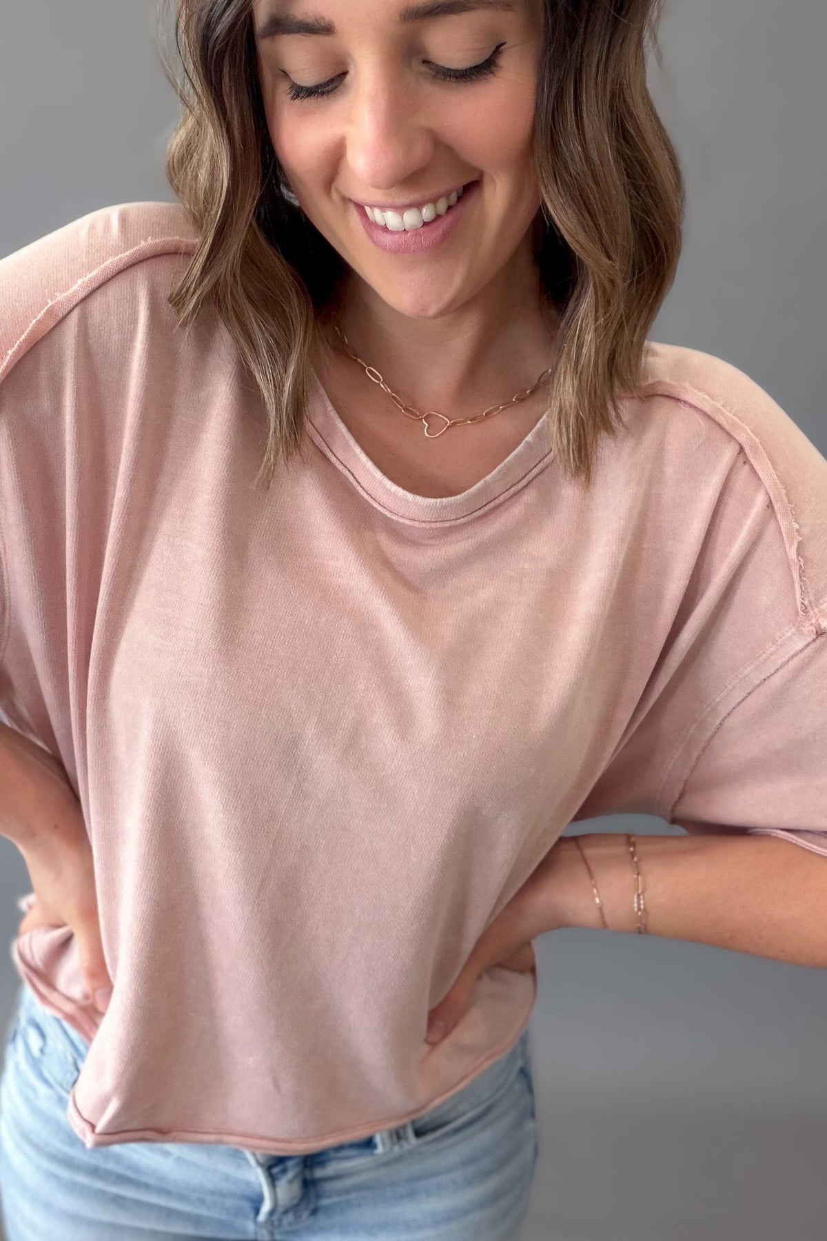 Woman wearing a light pink tee with blue jeans on a grey background
