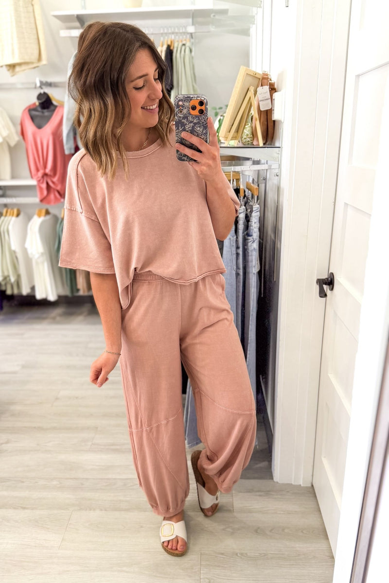 Woman taking a mirror selfie wearing a pink outfit set in a clothing store.