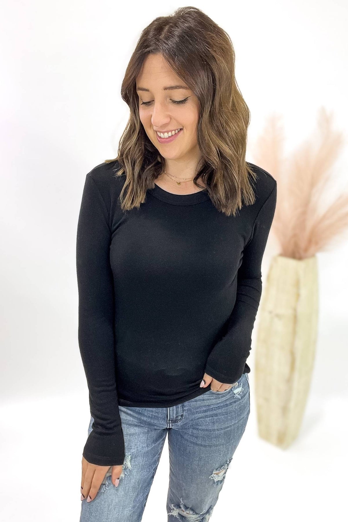 Woman wearing a black long-sleeve top and blue jeans against a white background