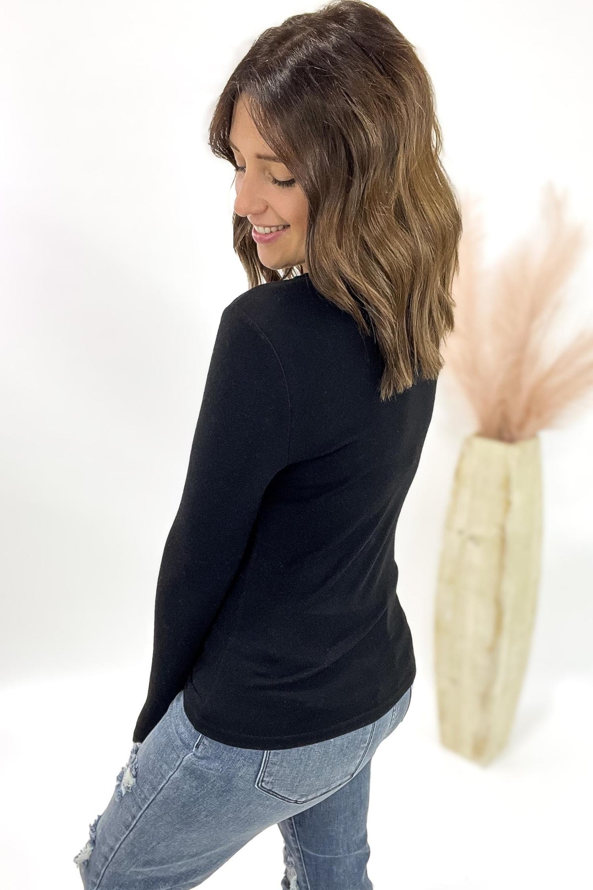 Woman wearing a black long-sleeve top and blue jeans, standing against a white background.