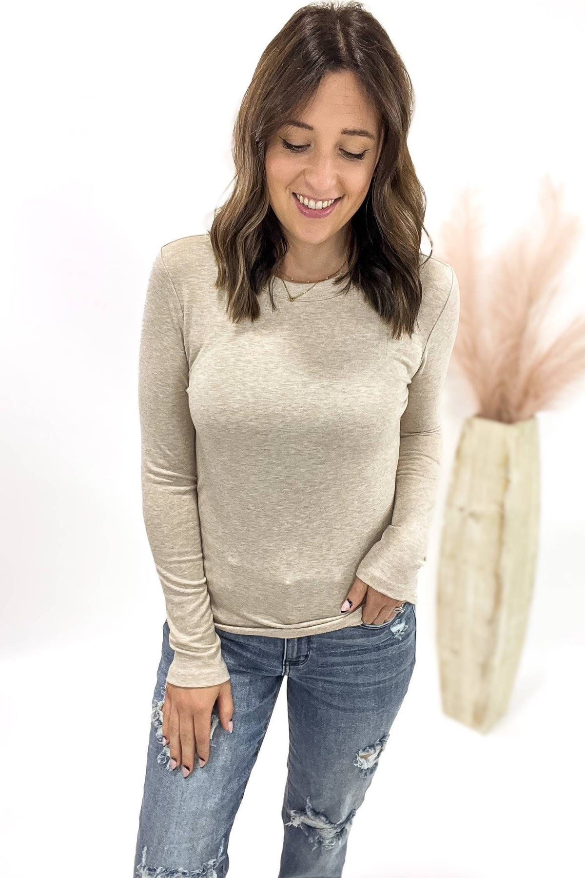 Woman wearing a oatmeal long-sleeve top and blue jeans on a white background