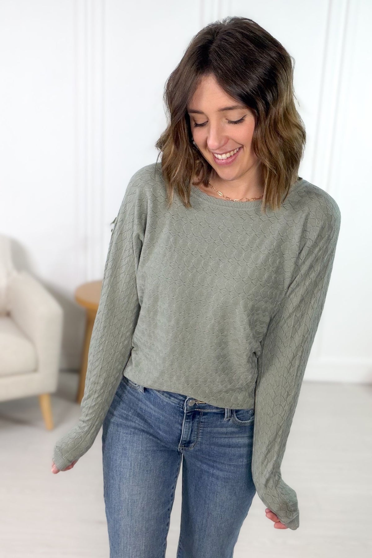 woman wearing a sage diamond pattern sweater with scalloped details styled with blue denim jeans