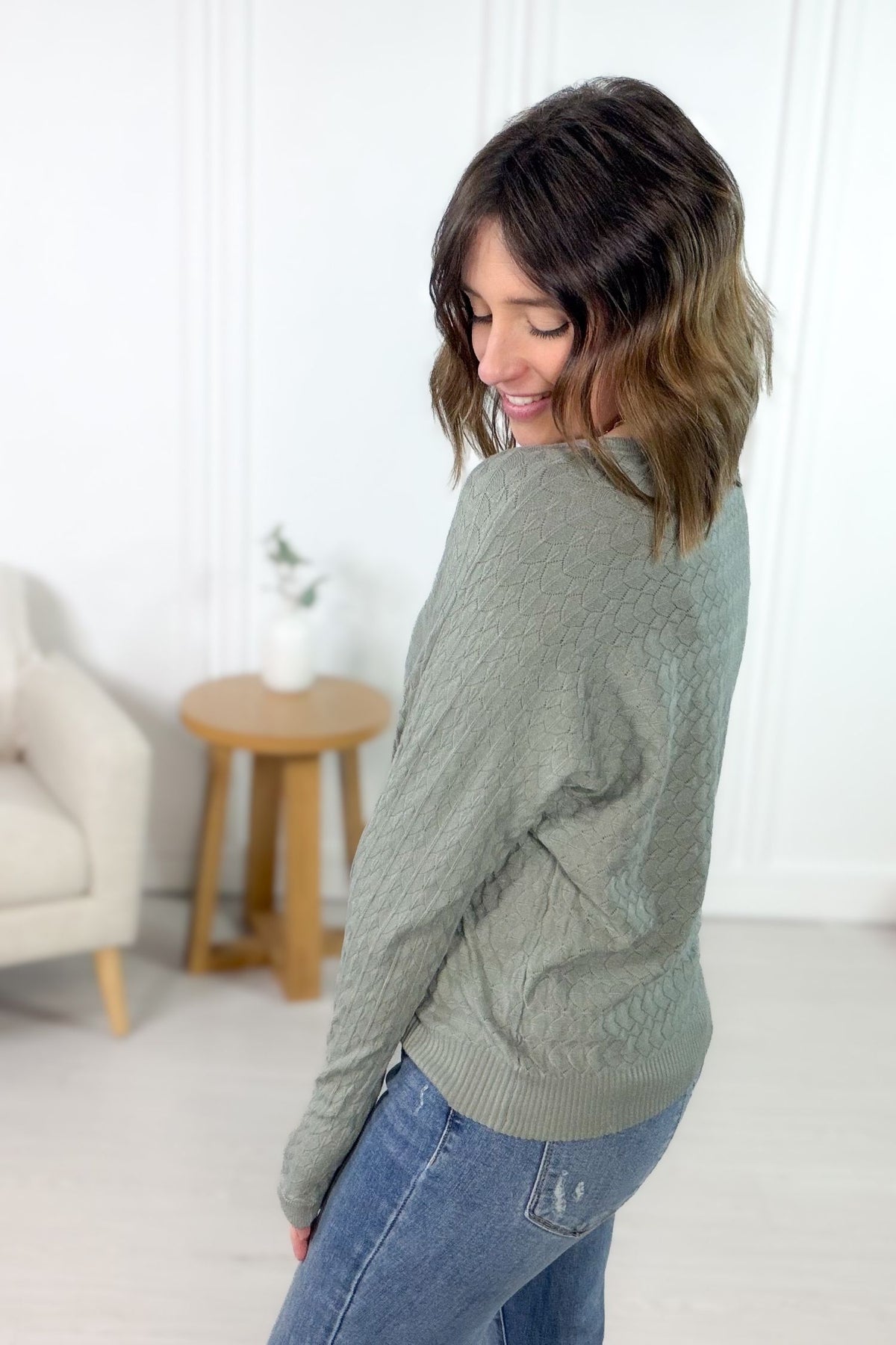 Sage diamond pattern sweater with scalloped details styled with blue denim jeans showing side/back details.