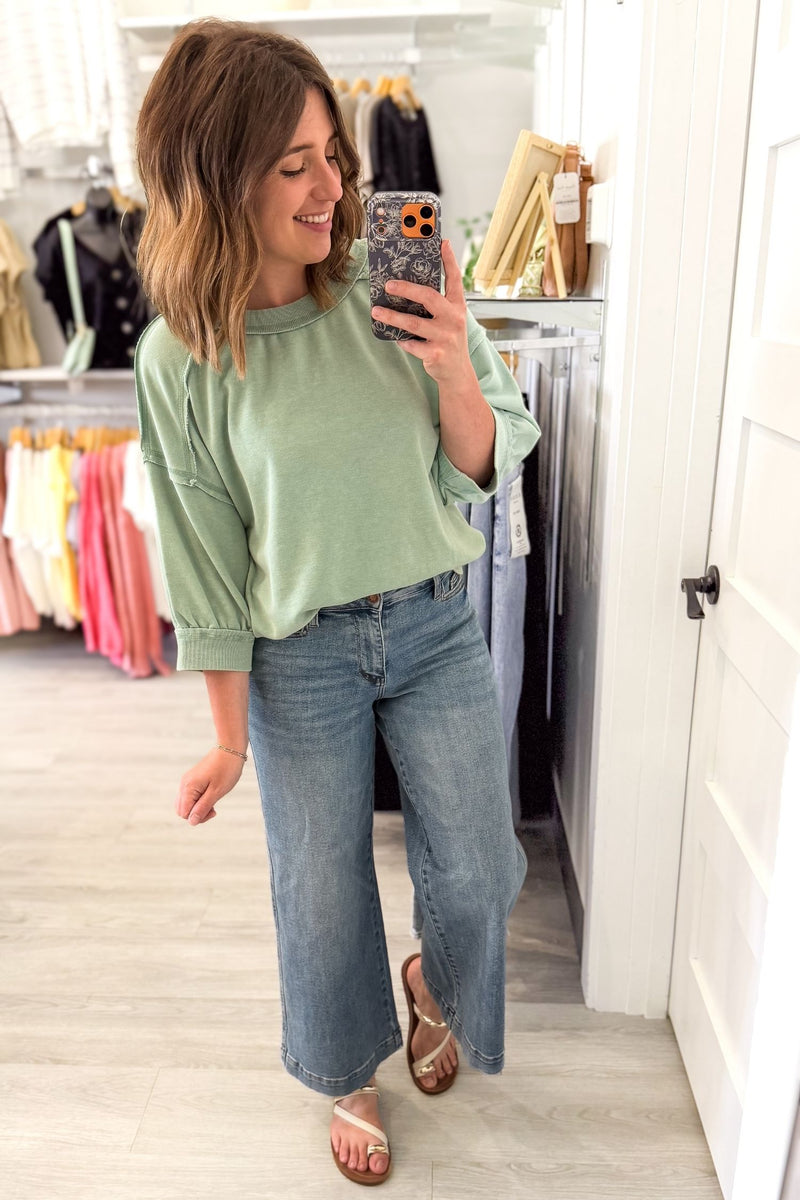 woman taking a mirror selfie wearing a soft french terry lounge top with blue jeans and sandals in a boutique
