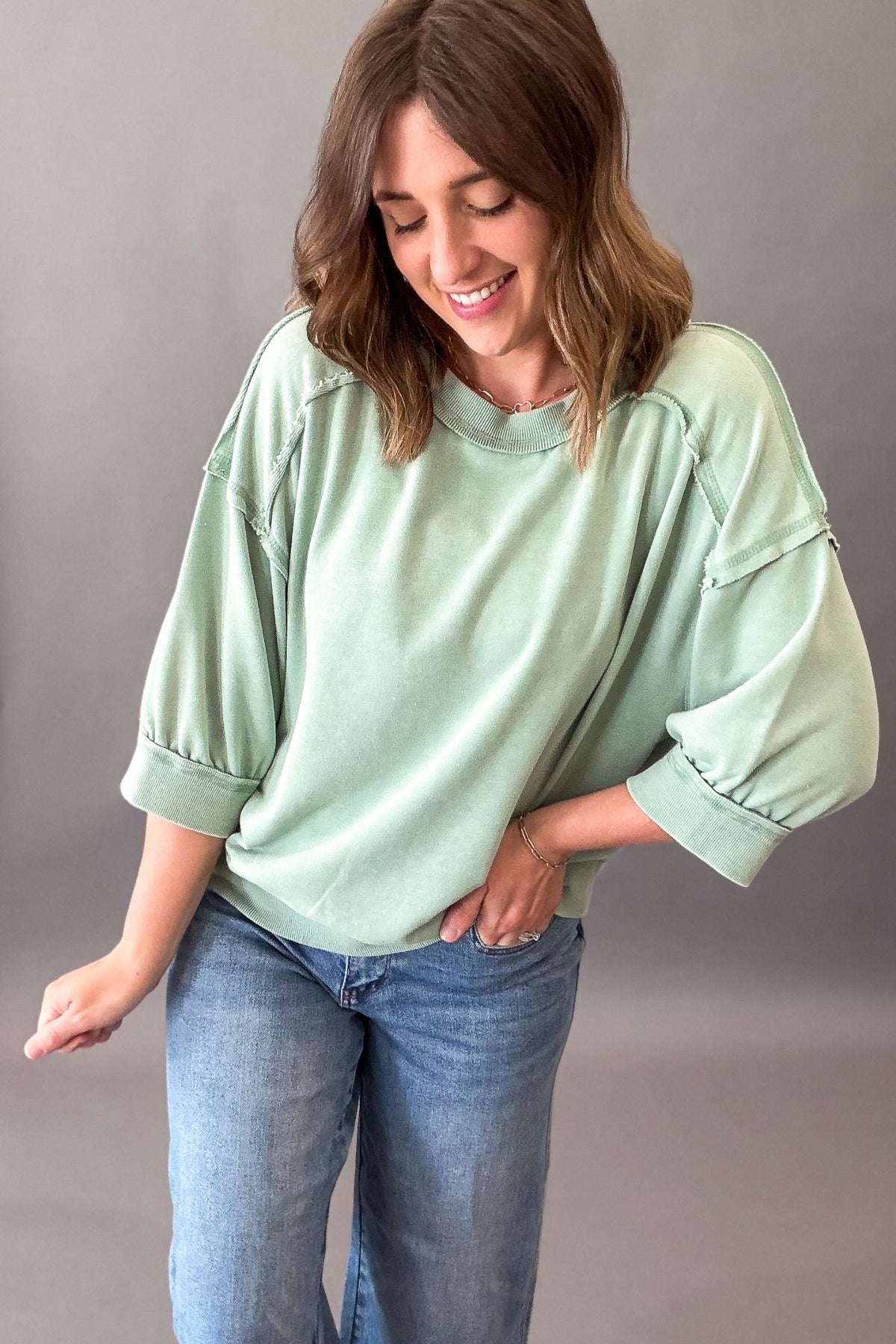 Woman wearing a light green oversized short sleeve and blue jeans against a gray background