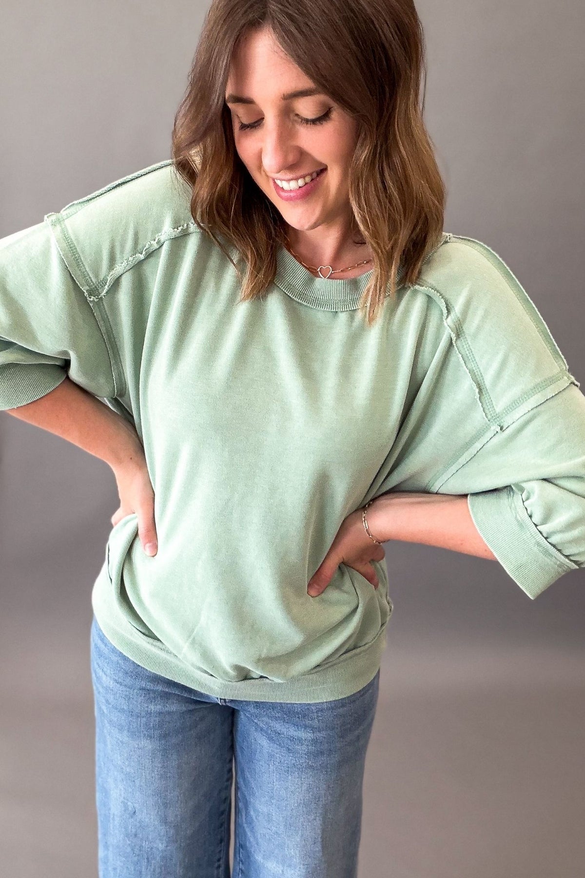 Woman wearing a light green oversized short sleeve and blue jeans against a gray background