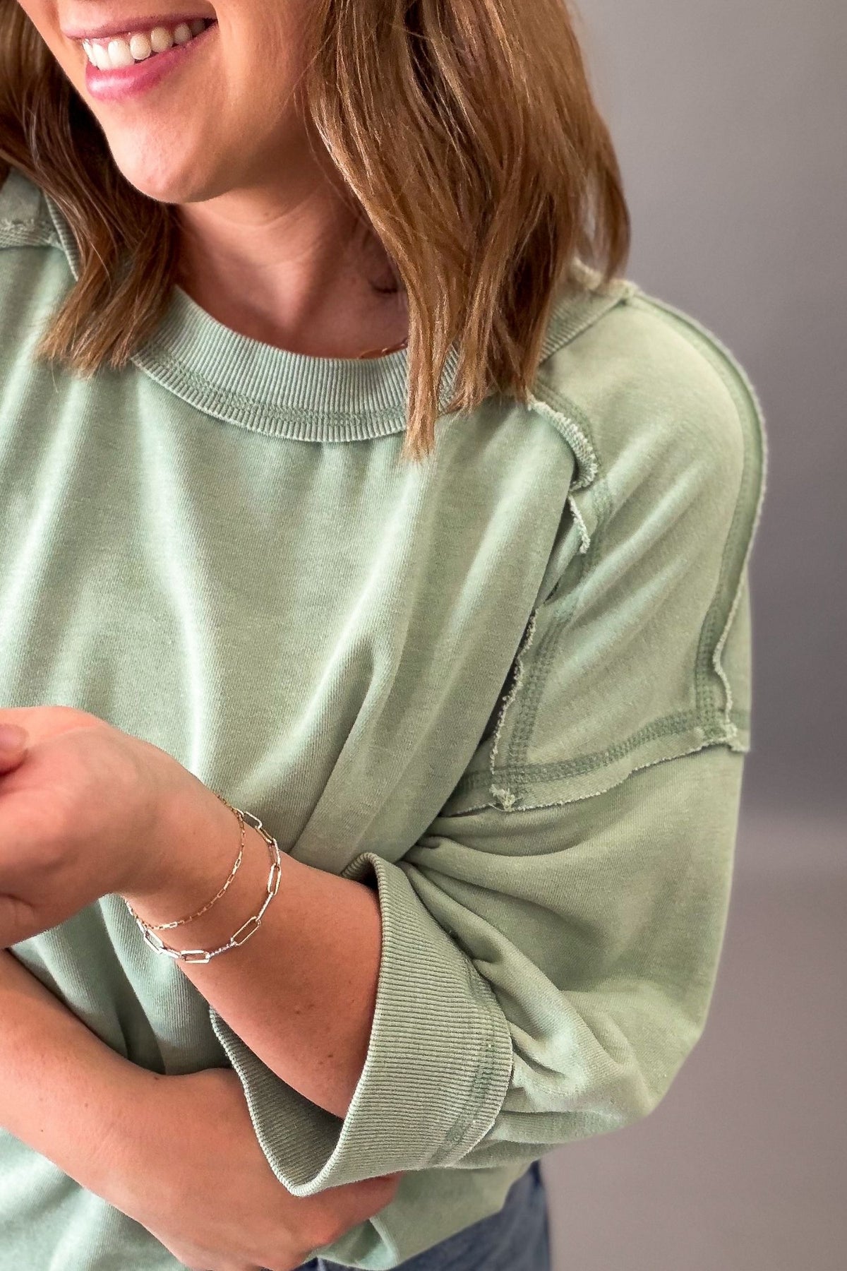 woman wearing a sage green french terry lounge top showing the texture and seam detail on the short sleeve