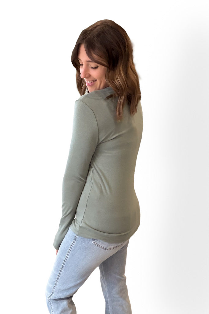 Woman wearing a green long-sleeve top and light blue jeans on a white background