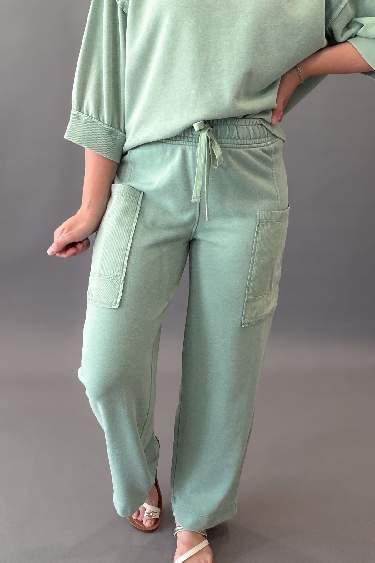 woman wearing a sage green lounge pocket pant with the matching short sleeve on a grey background