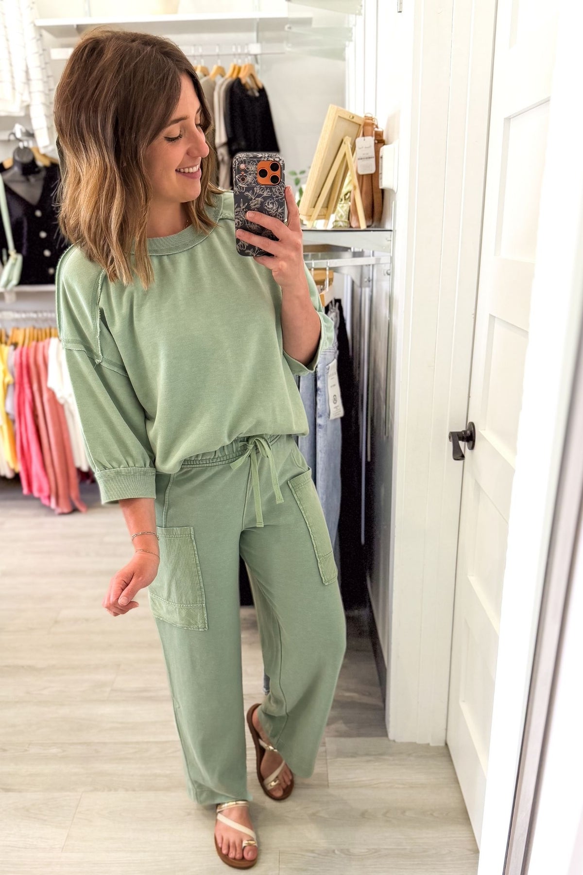 woman taking a mirror selfie wearing a sage french terry lounge set in a boutique setting