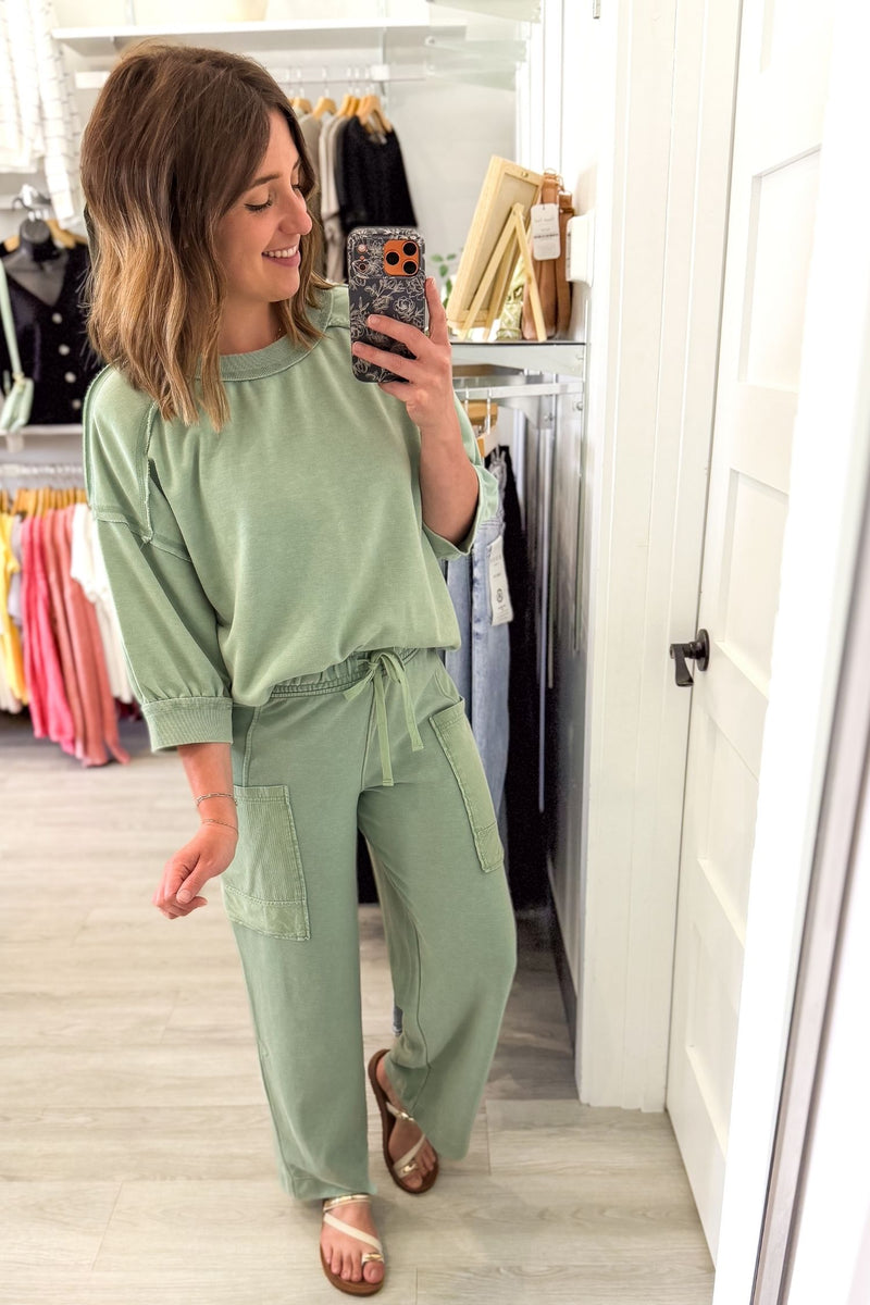 woman taking a mirror selfie wearing a sage french terry lounge set in a boutique setting