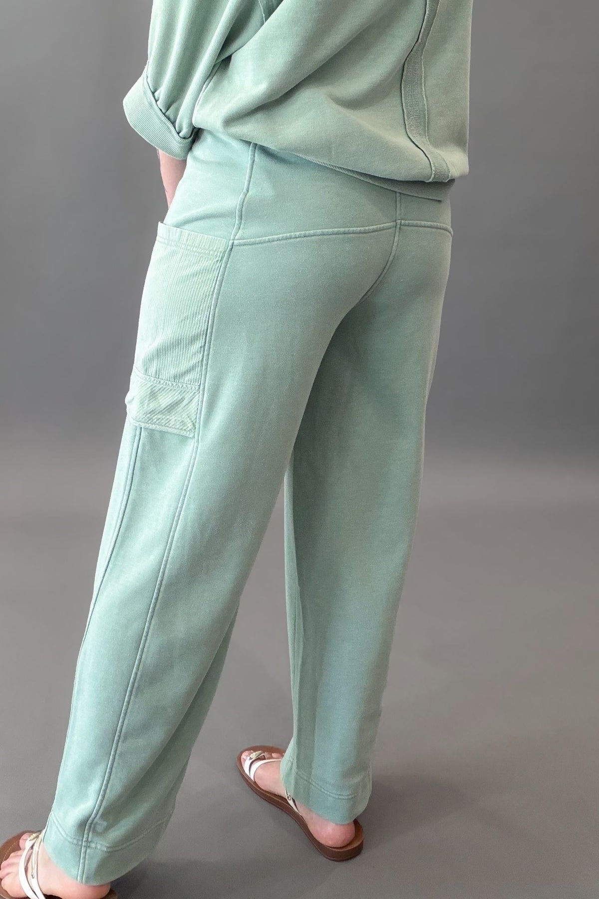 woman wearing a light green sage lounge pocket pants with the matching top against a charcoal background