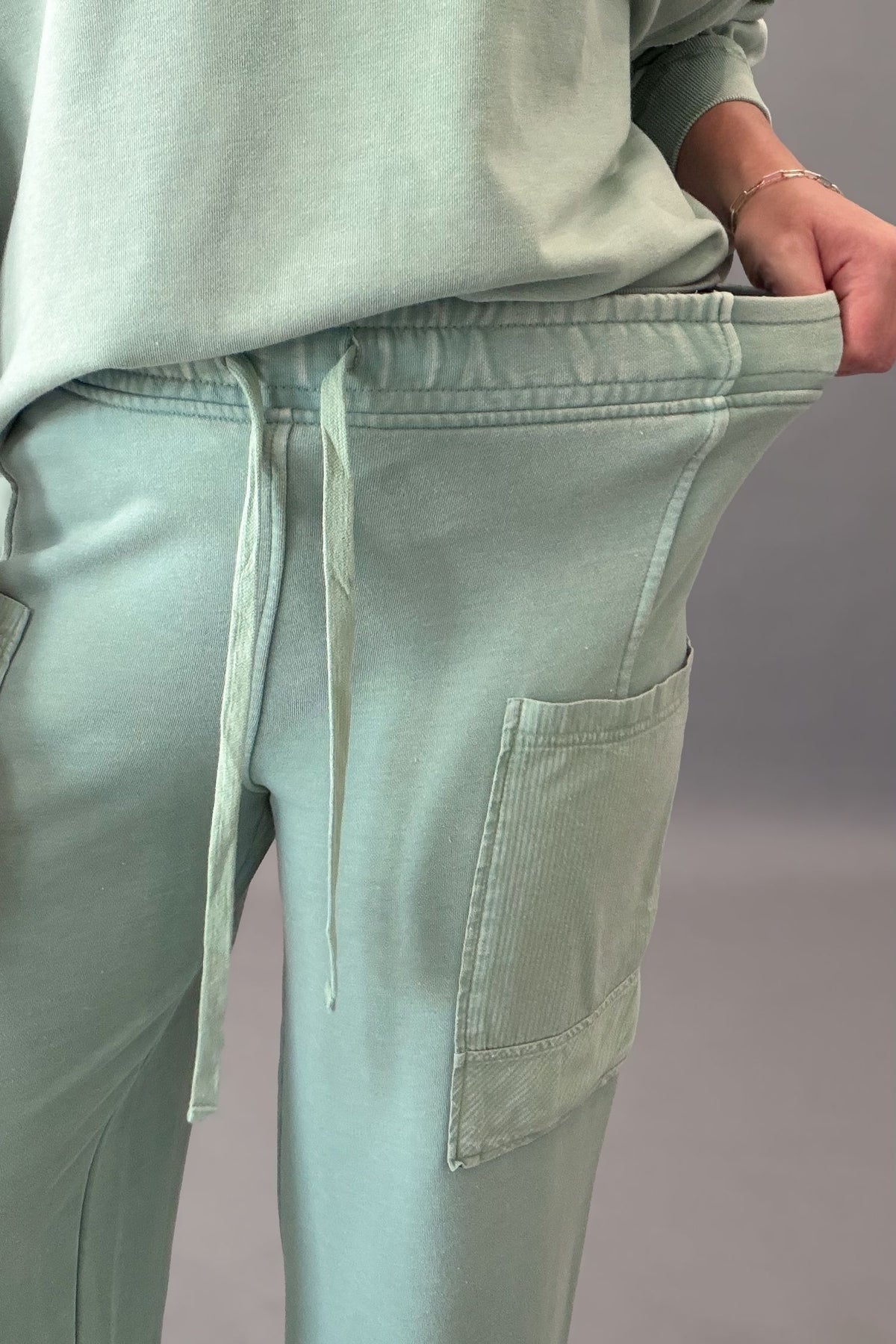 woman wearing a light green french terry drawstring pant showing the stretch 