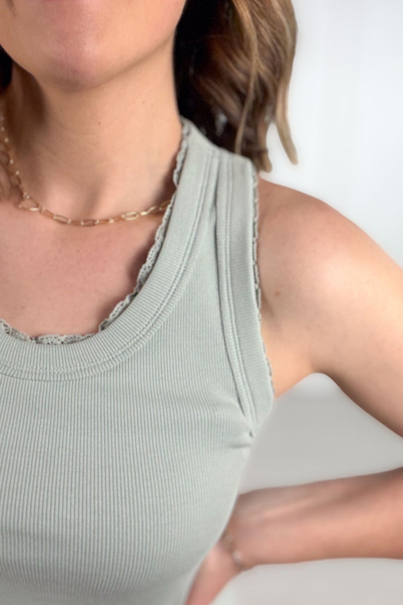 Woman wearing a sage tank with lace trim details paired with white denim.