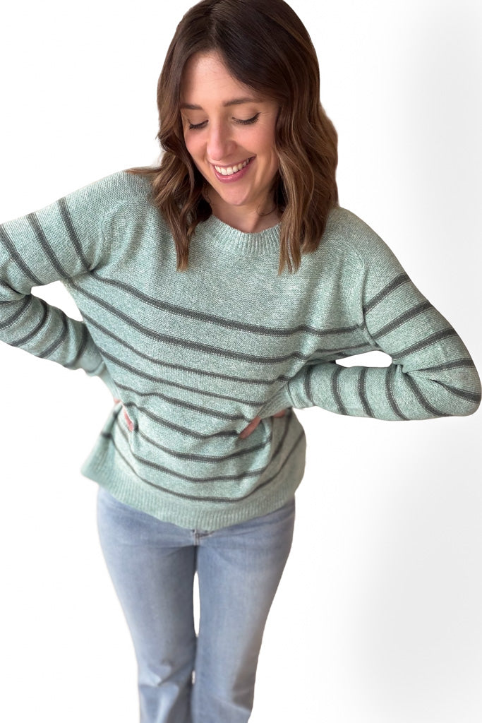 woman wearing a sage striped long sleeve  with dark green stripes with blue jeans with a white background