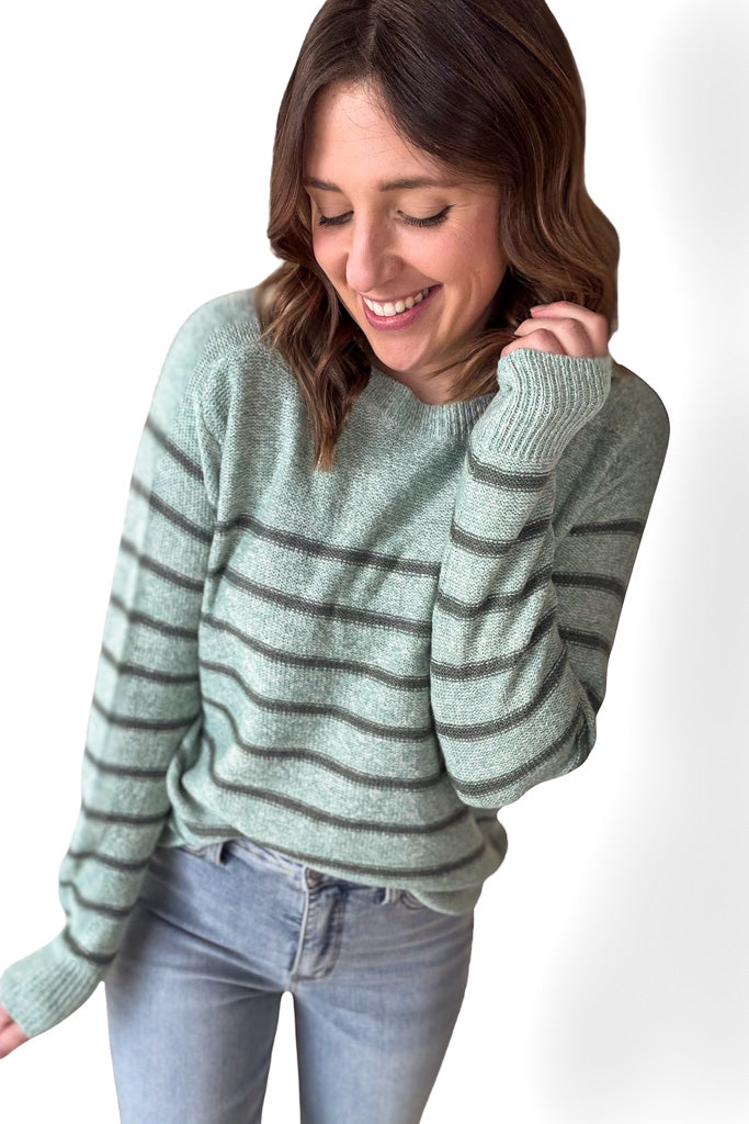 woman wearing a sage striped long sleeve  with dark green stripes with blue jeans with a white background