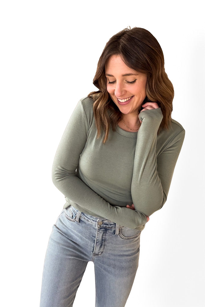 Woman wearing a tailored green long sleeve with blue jeans against a white background