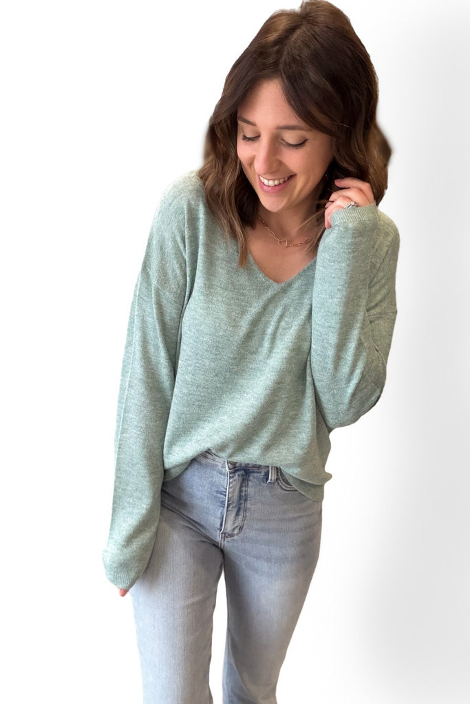 Woman wearing a light green sweater and light blue jeans against a white background