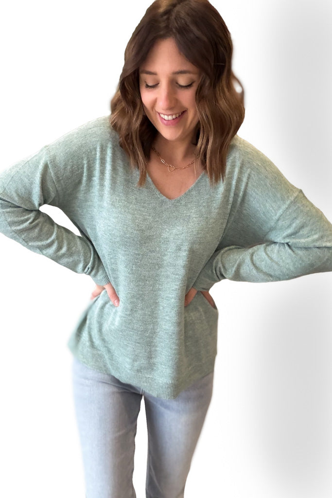 Woman wearing a light green sweater and light blue jeans against a white background