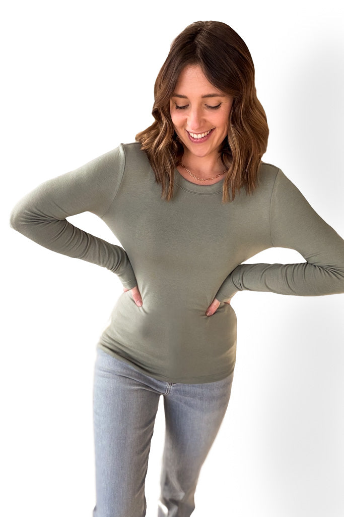 Woman wearing a tailored green long sleeve with blue jeans against a white background