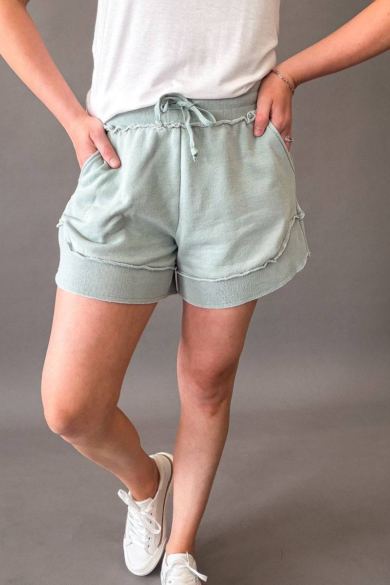 woman wearing french terry shorts with sneakers on a grey background showing side pockets