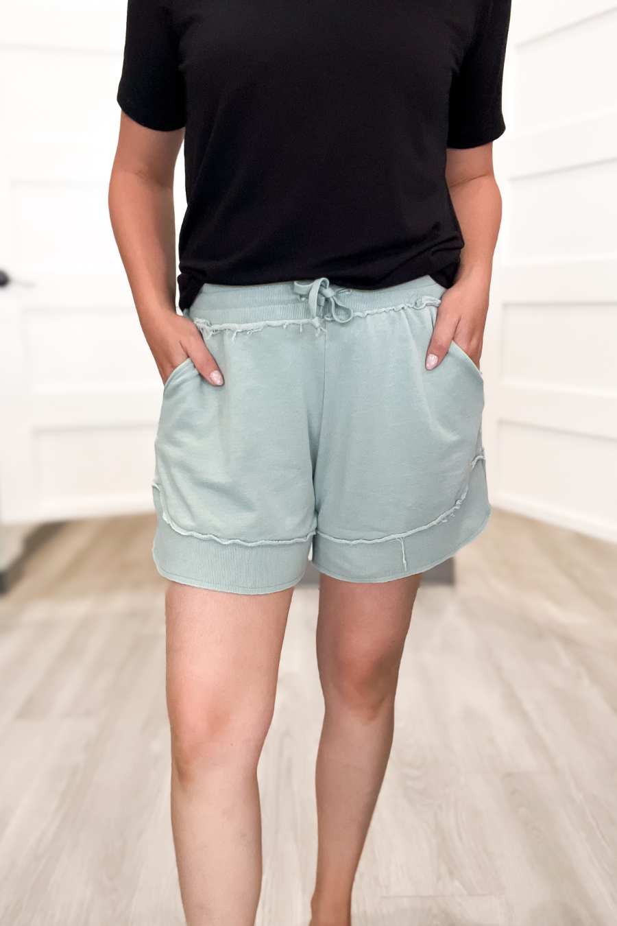 Person wearing light blue shorts and a black top on a neutral background