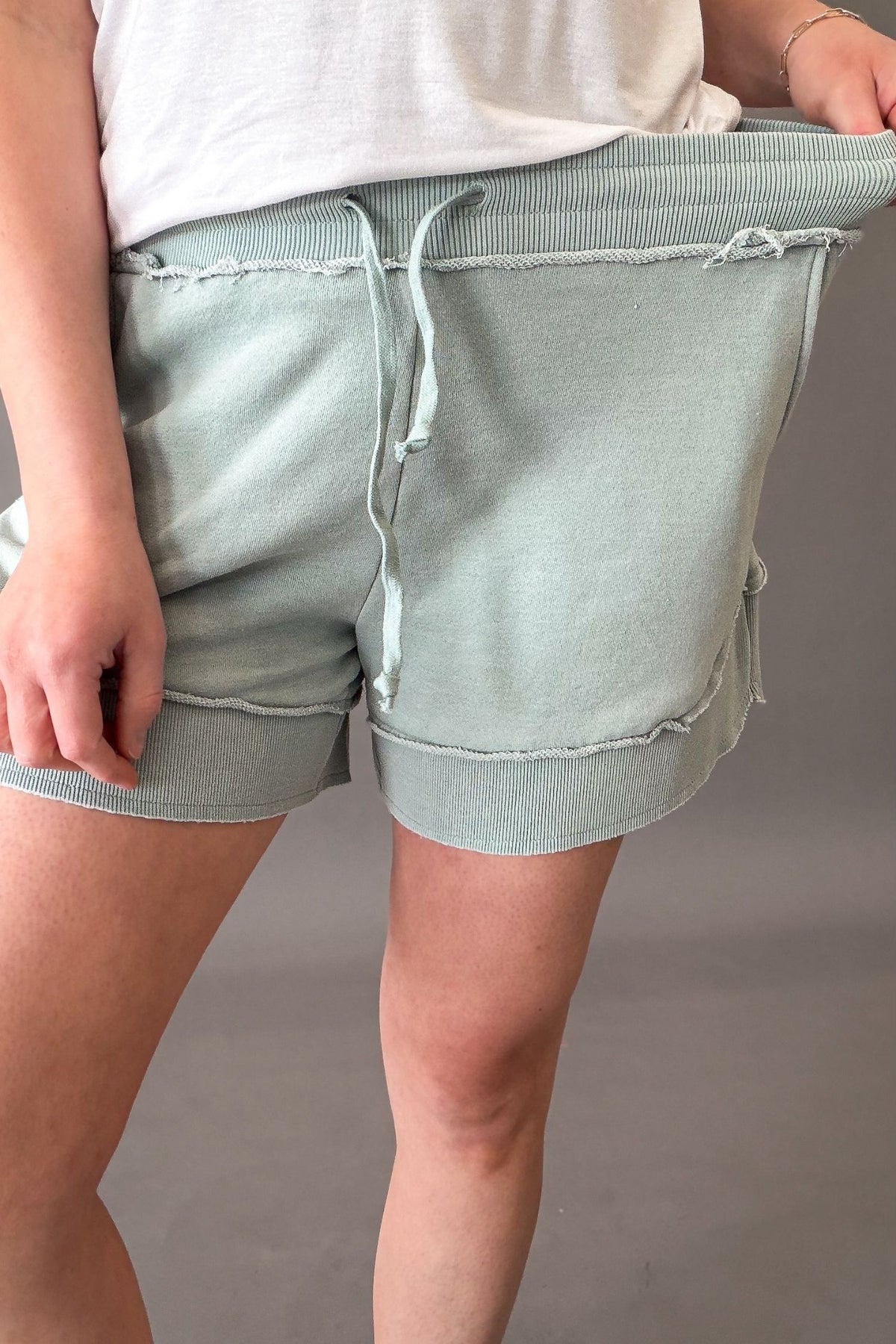 woman wearing french terry shorts with sneakers on a grey background showing stretch in waistband.