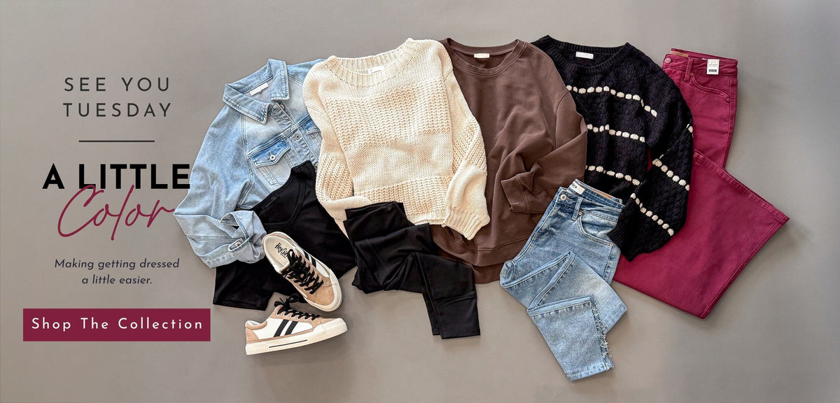 A styled flat-lay of multiple clothing items on a neutral gray background, including a cream knit sweater, brown top, black patterned sweater, denim jacket, jeans, black pants, burgundy pants, and sneakers. Text on the left reads 'SEE YOU TUESDAY', 'A LITTLE Color', and 'Shop The Collection'.
