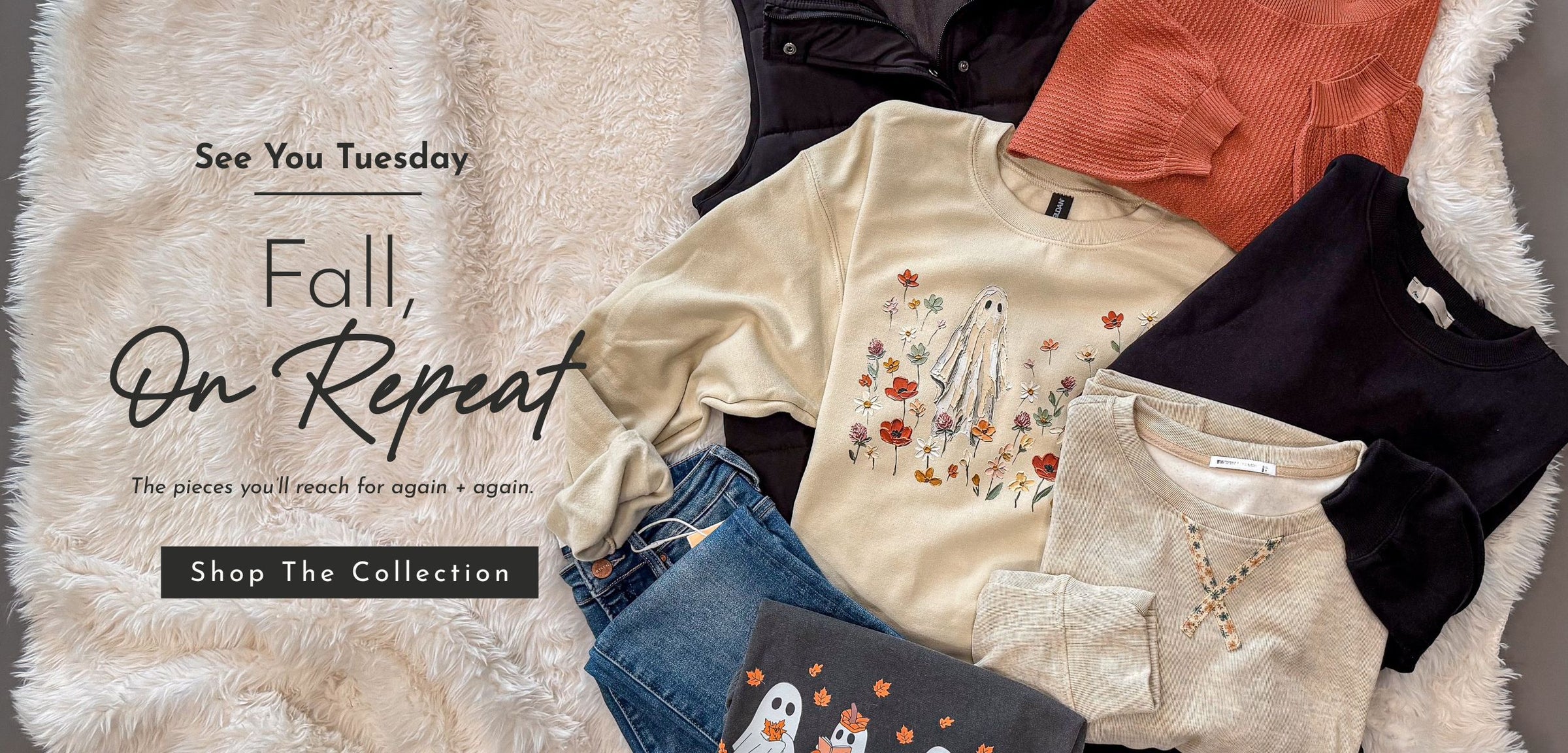 A styled flat lay of multiple women's clothing pieces arranged on a white faux-fur surface with promotional text reading 'See You Tuesday Fall, On Repeat' and 'Shop The Collection.' Visible items include a cream long-sleeve top with a ghost floral print, a coral ribbed top, a dark navy top, a light beige knit top, blue jeans, and a dark gray top with a ghost graphic.