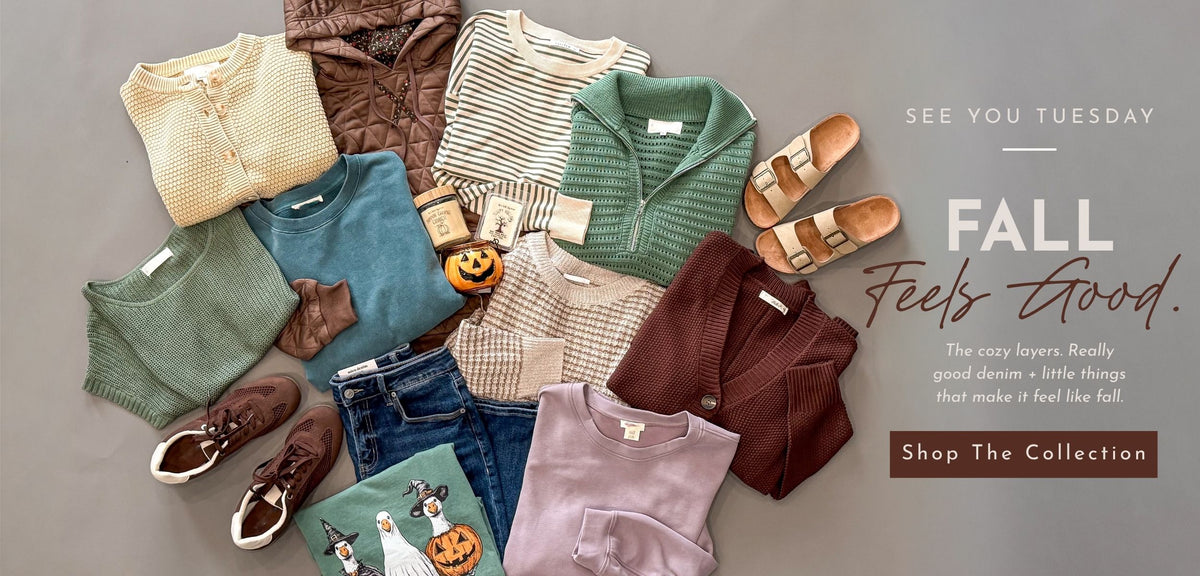 A styled flat lay of multiple folded and laid-out clothing items in muted fall colors on a gray background, including cardigans, tops, jeans, shoes, and a small pumpkin decoration. Text on the right reads 'SEE YOU TUESDAY FALL Feels Good.