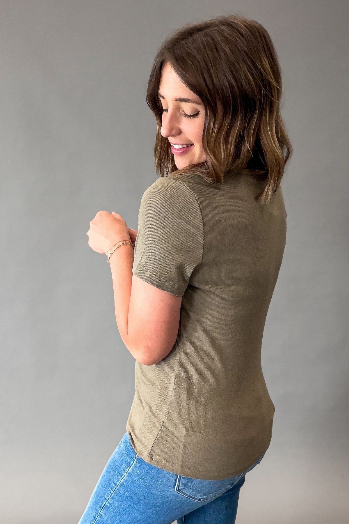 woman wearing a olive ribbed tee showing the back and side details of the fitted top.