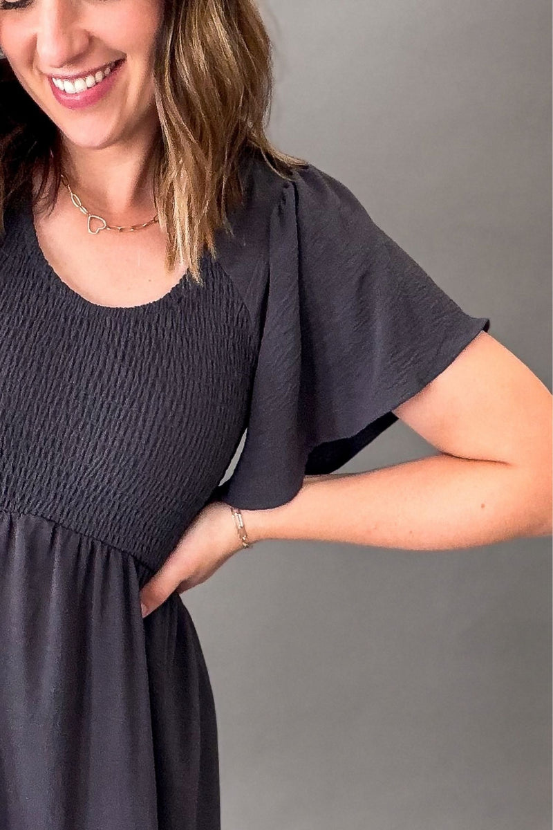woman wearing a smoky blue smocked bust dress with flutter sleeves, showing a closeup of the soft texture and smocked bust details.
