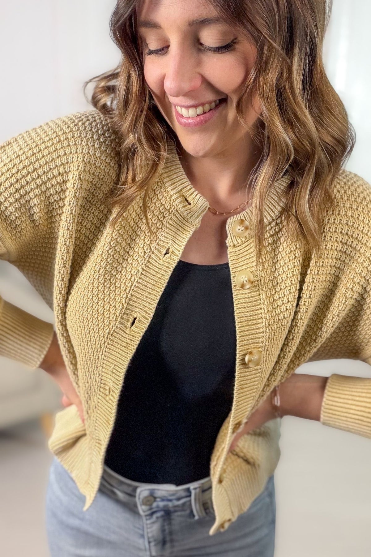 Woman wearing a soft camel knitted cardigan over a black top and blue jeans, smiling.