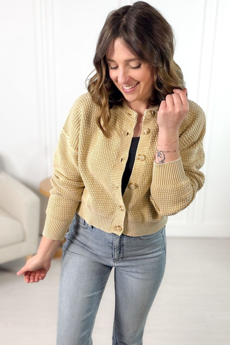 Woman wearing a soft camel knitted cardigan over a black top and blue jeans, smiling.