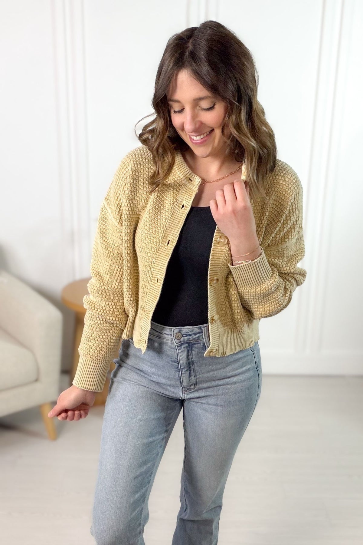 Woman wearing a soft camel knitted cardigan over a black top and blue jeans, smiling.