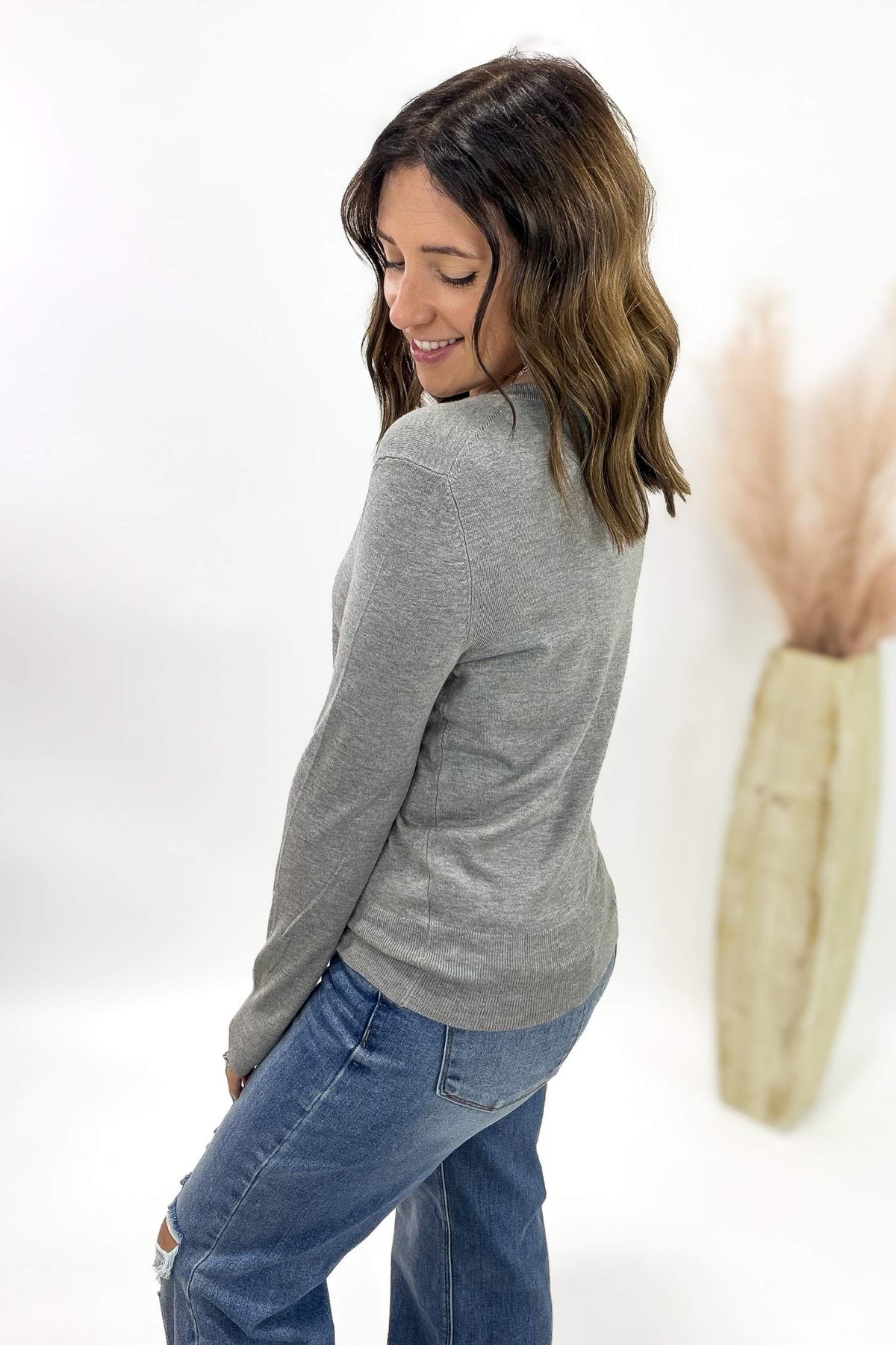 Woman wearing a gray sweater and blue jeans against a white background