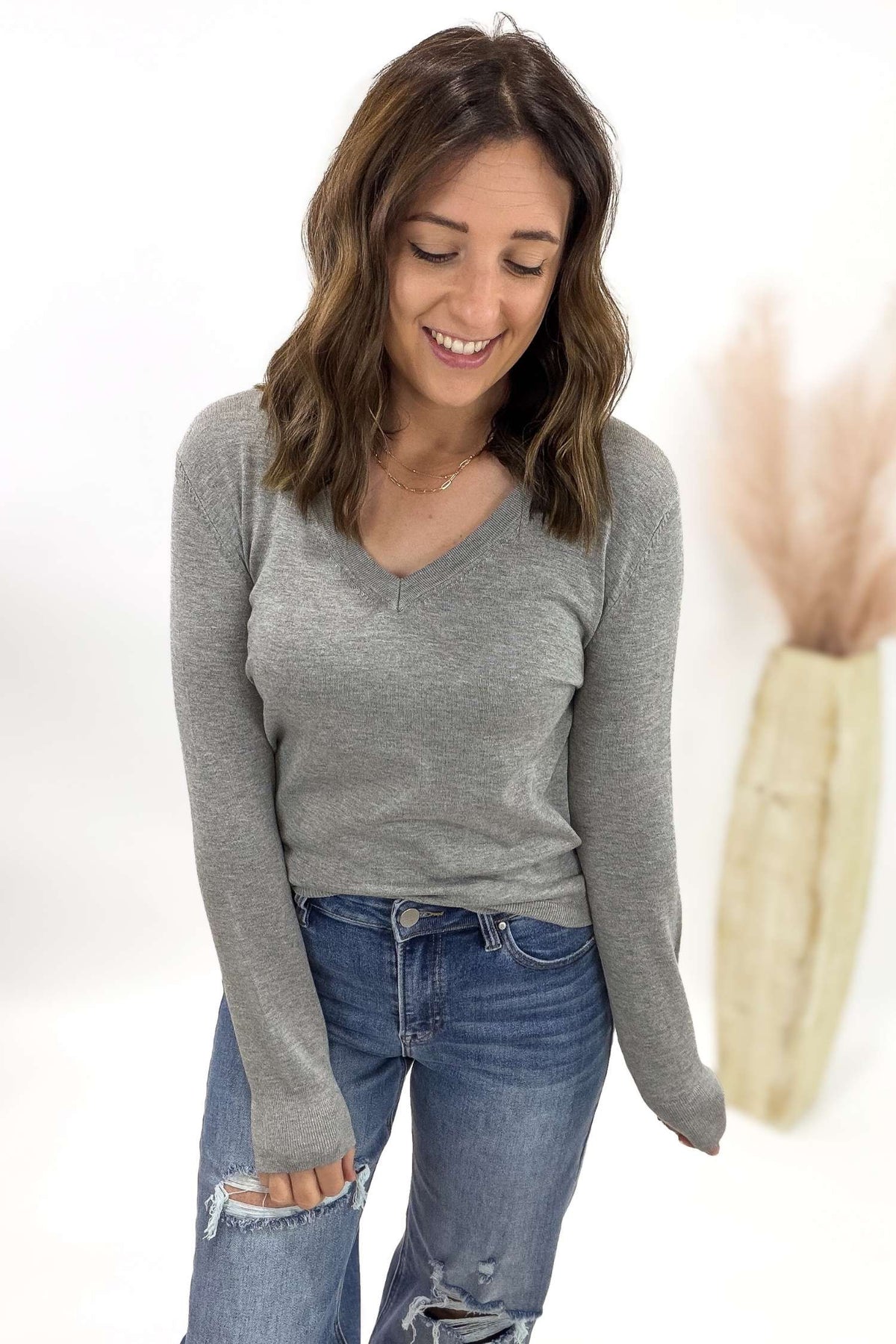 Woman wearing a gray long-sleeve top and blue jeans on a white background