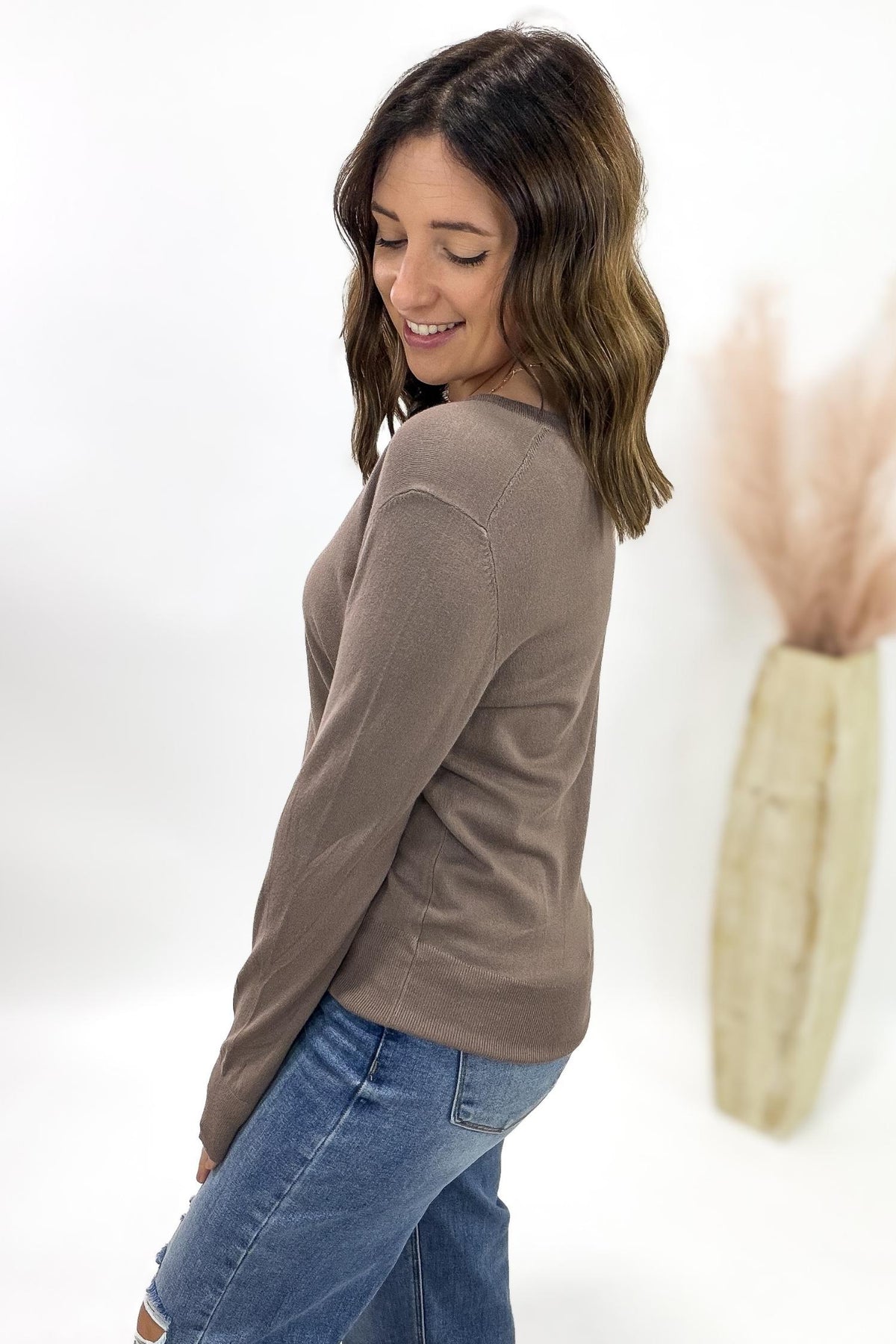 Woman wearing a brown long-sleeve top and blue jeans against a white background