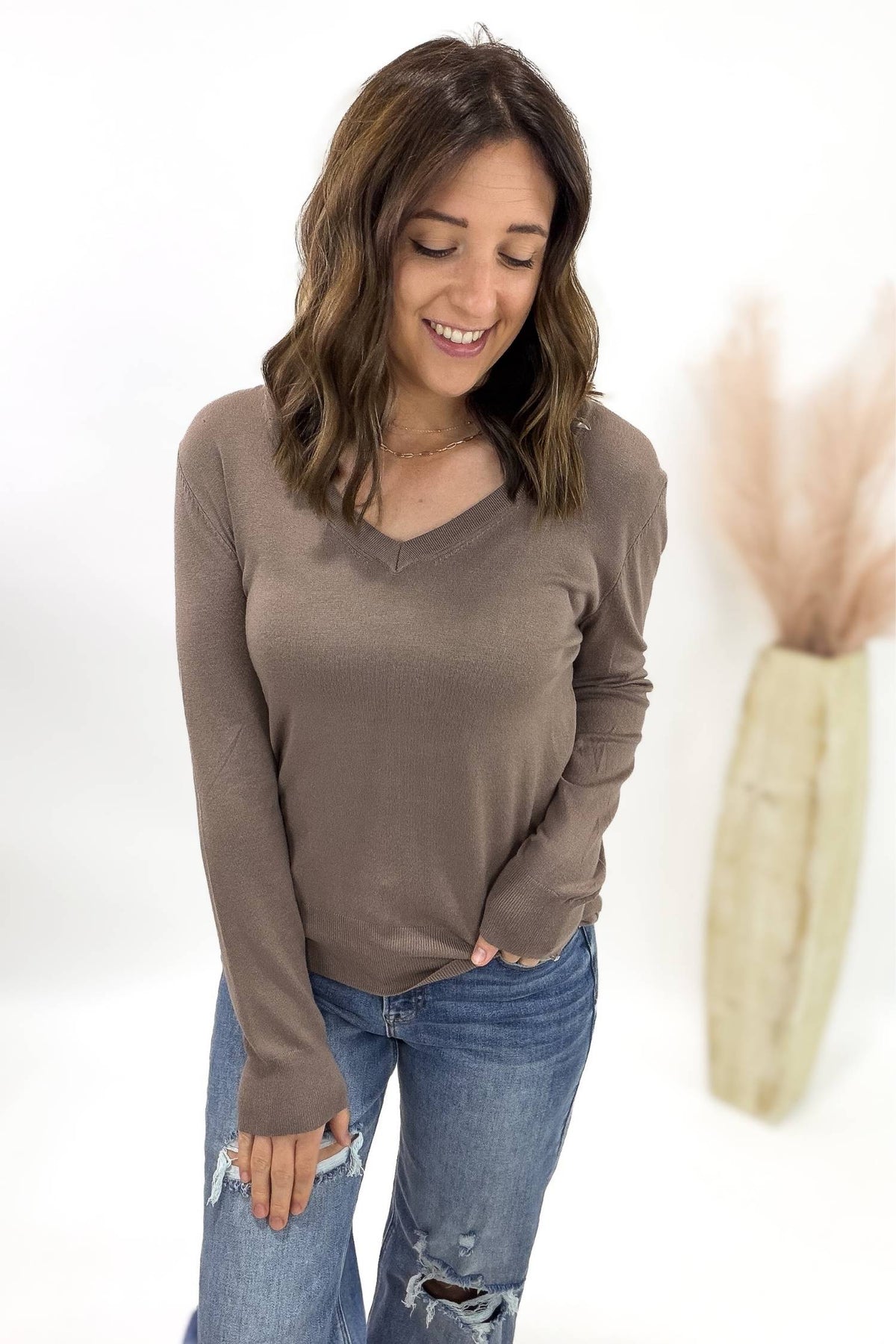 Woman wearing a brown long-sleeve top and blue jeans on a white background