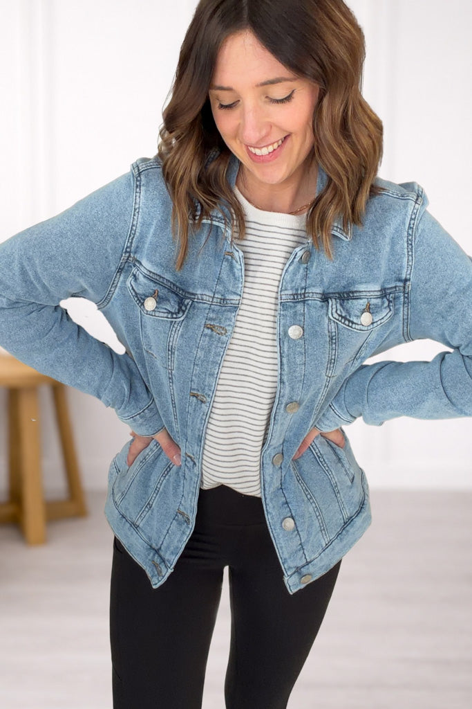 Woman wearing a denim jacket over a striped shirt with a white background