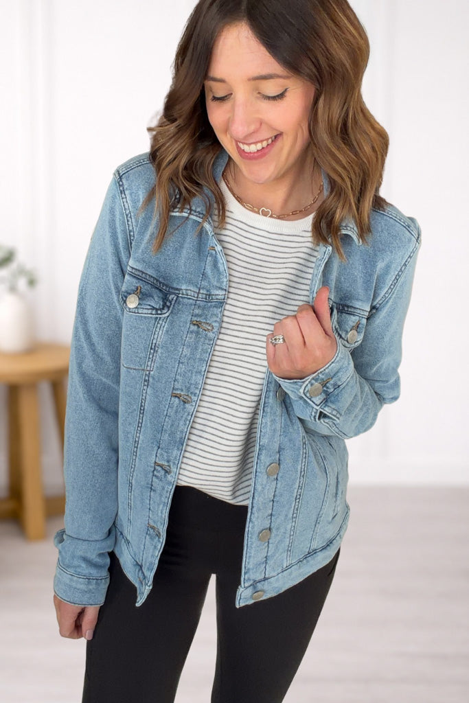 Woman wearing a denim jacket over a striped shirt with a neutral background