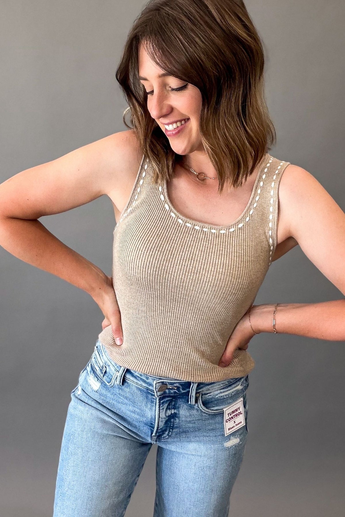 Woman wearing a soft mocha ribbed sweater tank with white contrast stitching styled with light wash RISEN jeans.