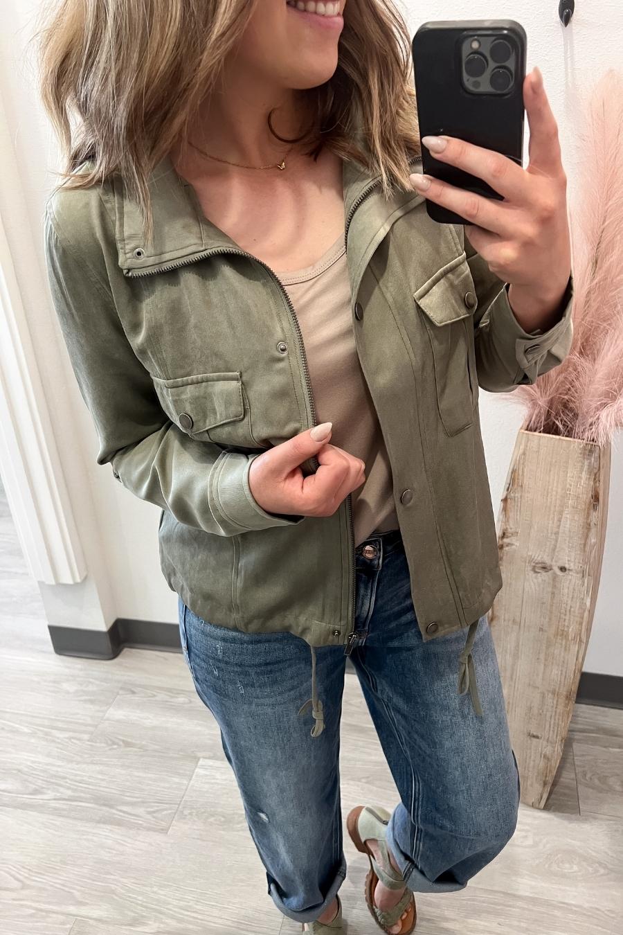 Person wearing a green jacket and blue jeans, taking a mirror selfie.