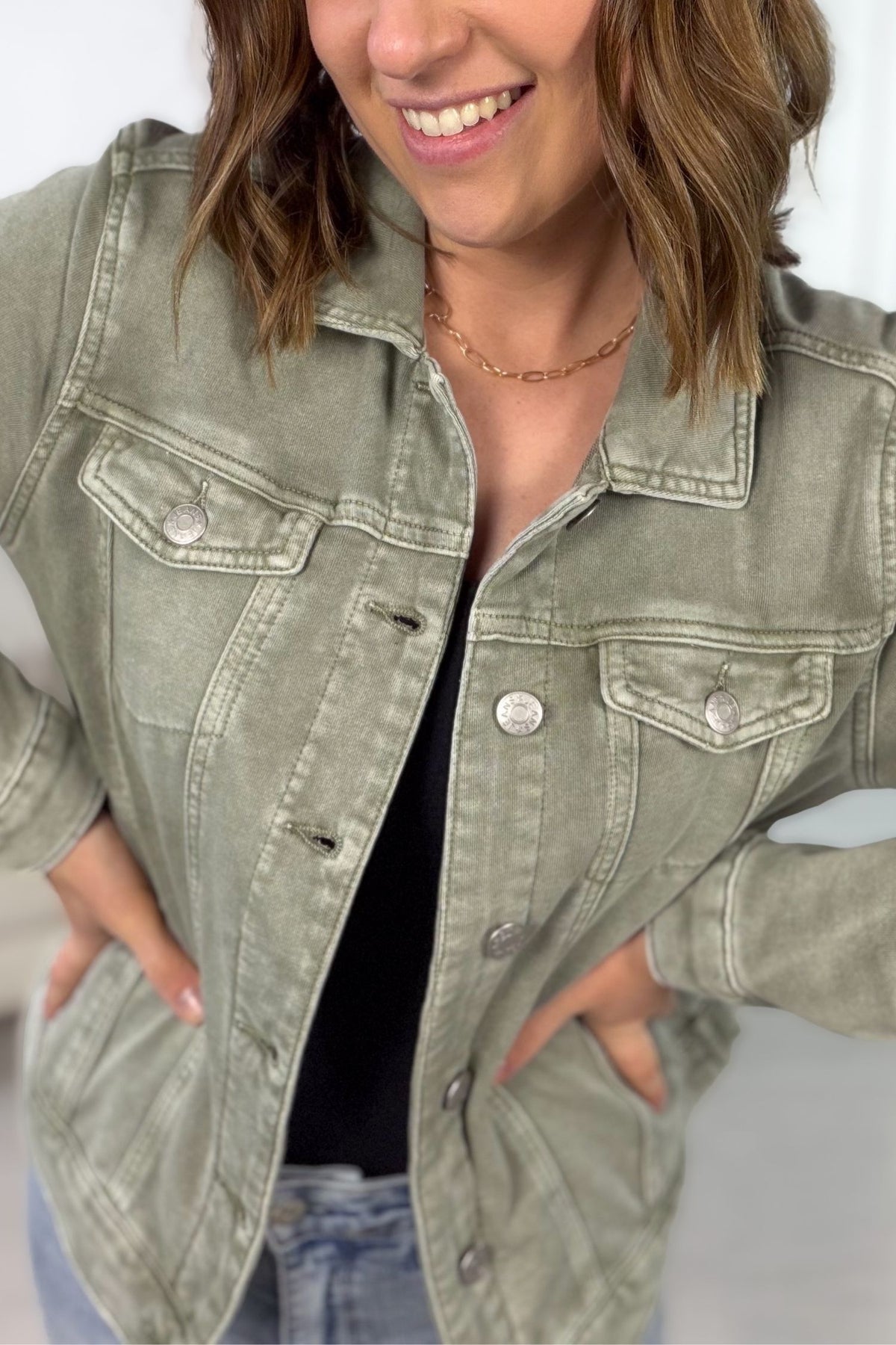 Person wearing a green denim jacket with a neutral background