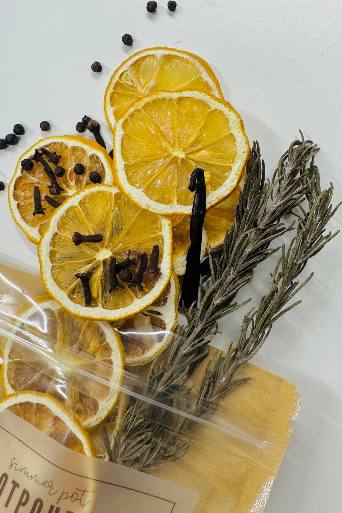 Dried lemon slices, rosemary, and black peppercorns in a clear bag on a white background
